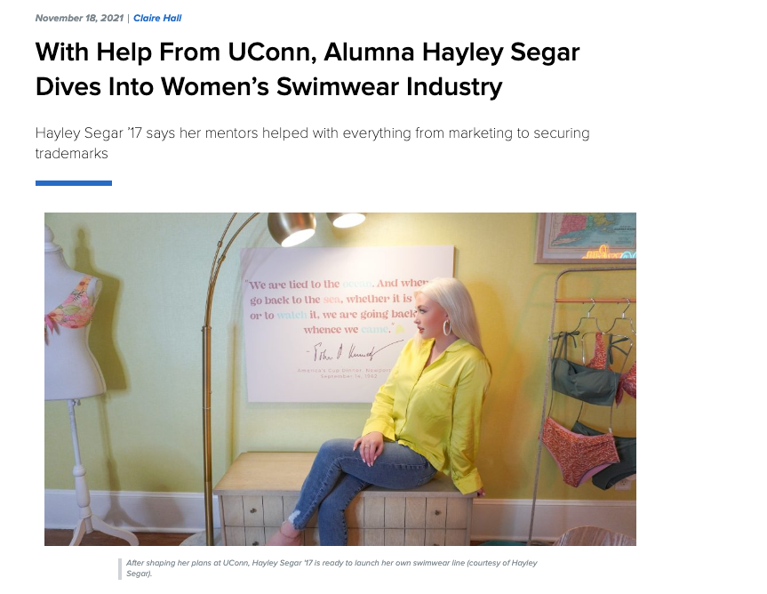 Hayley Segar seated in her swimwear design studio beside a mannequin and wall display of swim samples.