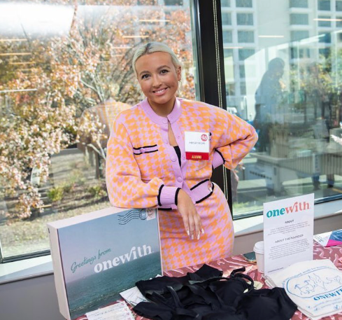 Smiling woman standing behind a table of packaged wellness products and signage at an indoor pop-up event.