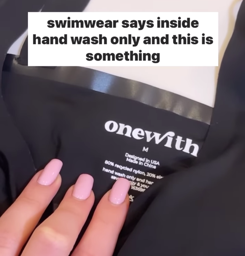 Hand on black swimsuit label 'onewith' size M; overlay reads: swimwear says inside hand wash only and this is something