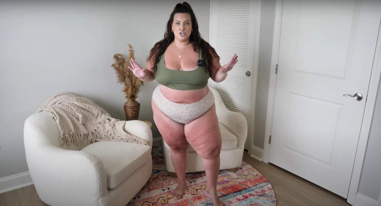 Plus-size model trying on onewith swim olive-green scoop-neck swim top and beige high-waisted patterned bottoms in a living room
