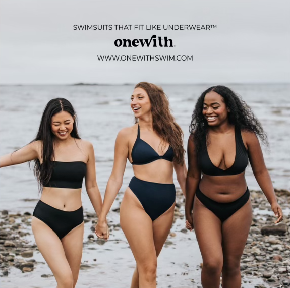 Three women in black swimsuits walking on a rocky beach; text: SWIMSUITS THAT FIT LIKE UNDERWEAR™ onewith WWW.ONEWITHSWIM.COM