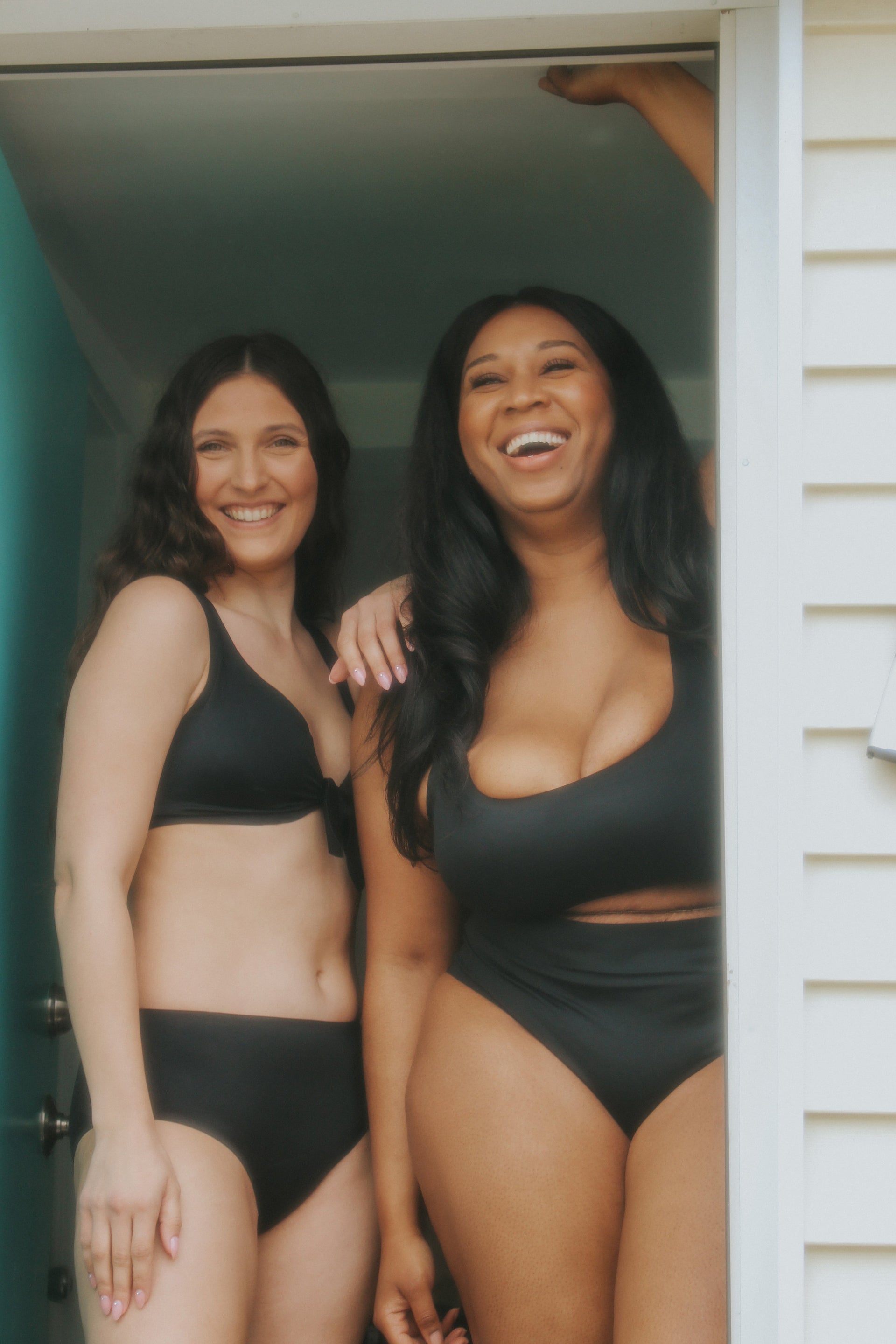 Two smiling women wearing black seamless swimwear standing in a doorway.