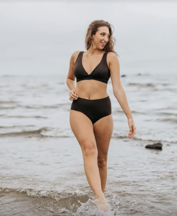Woman in a black seamless bikini walking on a beach, smiling, showing a flattering midsize fit.