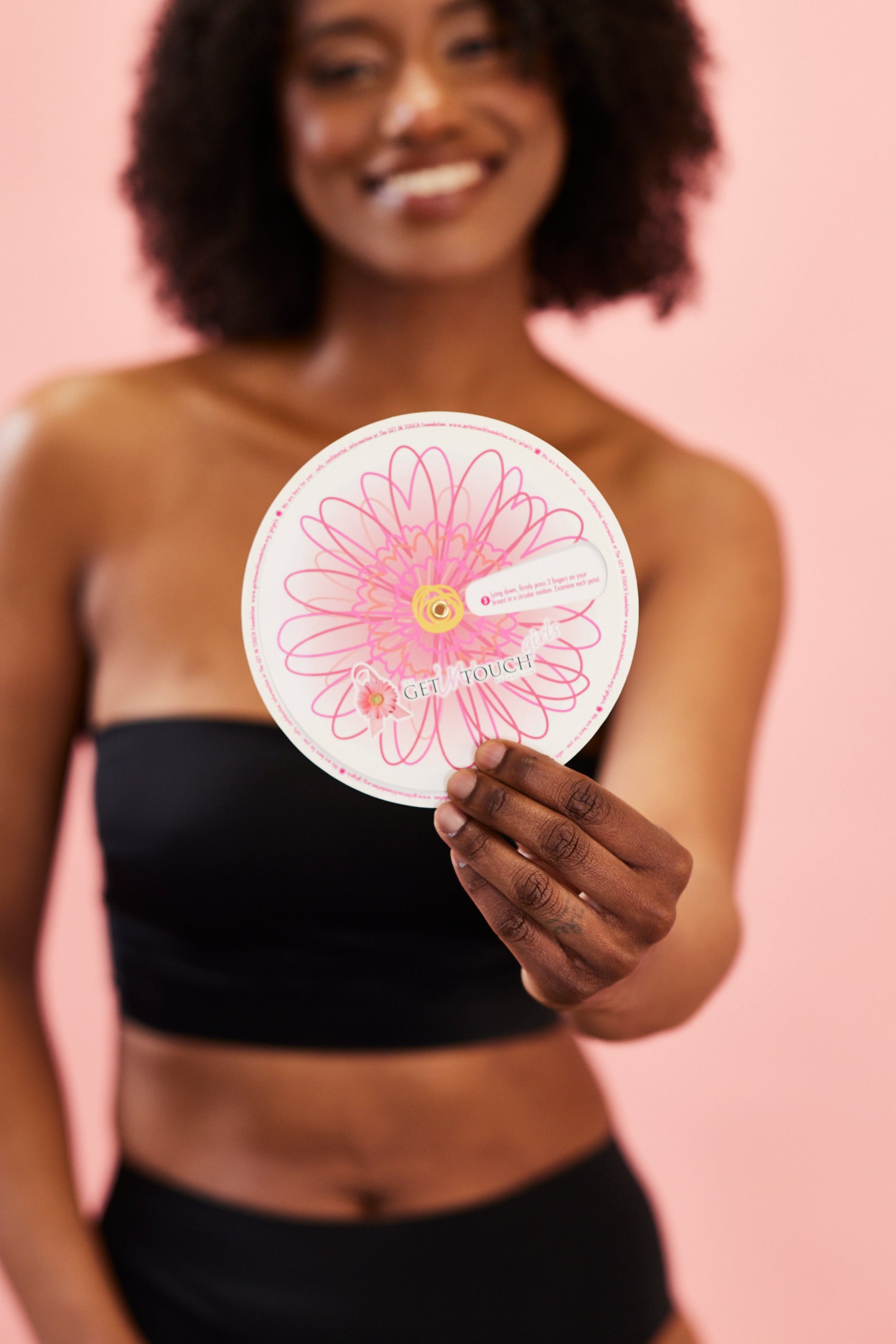 Woman holding round pink floral card that reads "GET IN TOUCH" against a pink background.