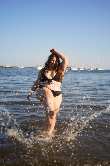 Woman in black bikini running and splashing through shallow sea water on a sunny beach.