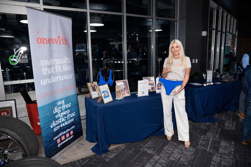 Onewith founder Hayley Segar holding a bright blue bikini bottom at an indoor booth with a onewith banner and product displays