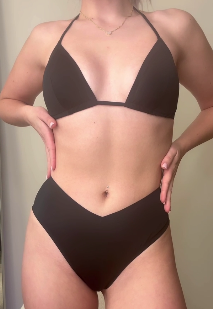 Person wearing a black triangle bikini top and high-cut V-waist bikini bottoms, hands on hips.