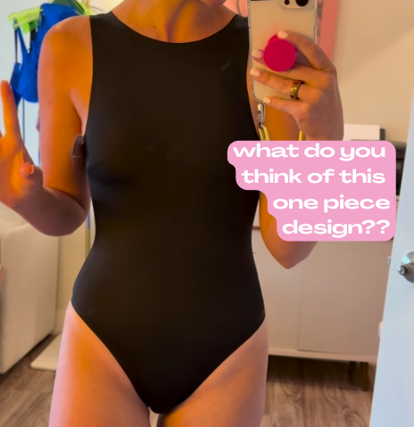 Mirror selfie wearing black high-cut one-piece; speech bubble what do you think of this one piece design??