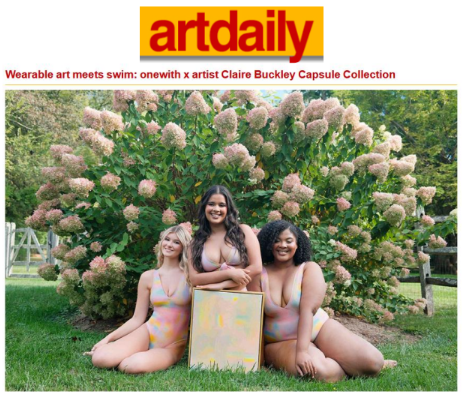 Three models seated on grass in colorful swimsuits holding a box, flowering bushes behind them with text banner: artdaily. Wearable art meets swim: onewith x Claire Buckley Capsule Collection