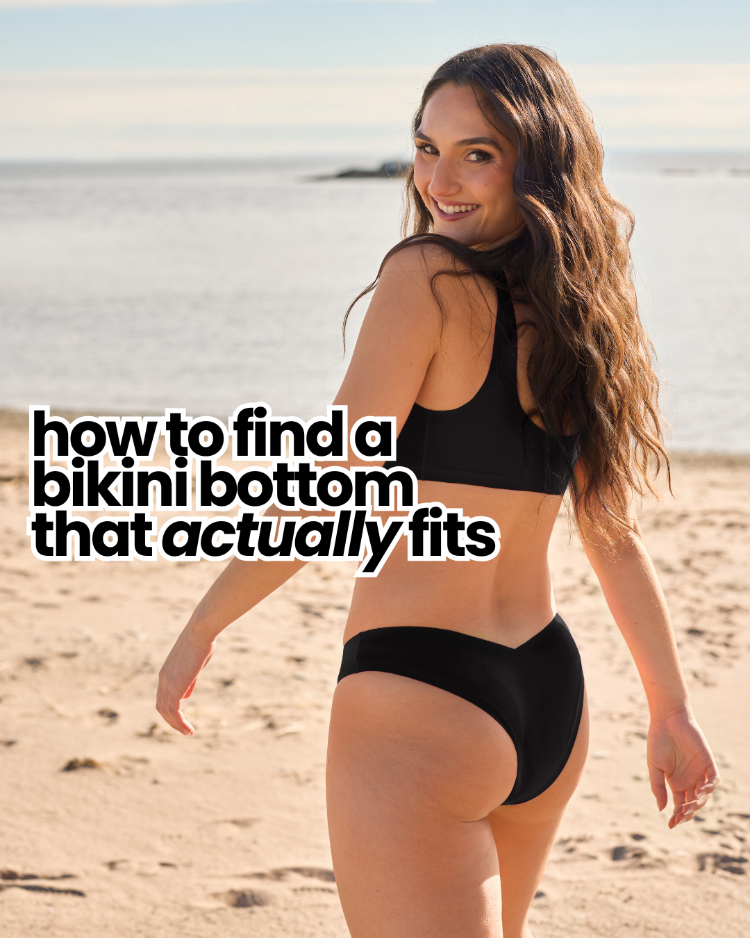 Smiling woman looking over her shoulder on a beach wearing a black V-cut cheeky bikini bottom and matching top