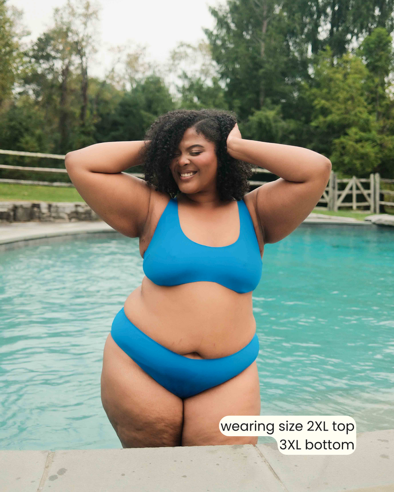 Woman in a blue bikini standing in a pool with trees in the background