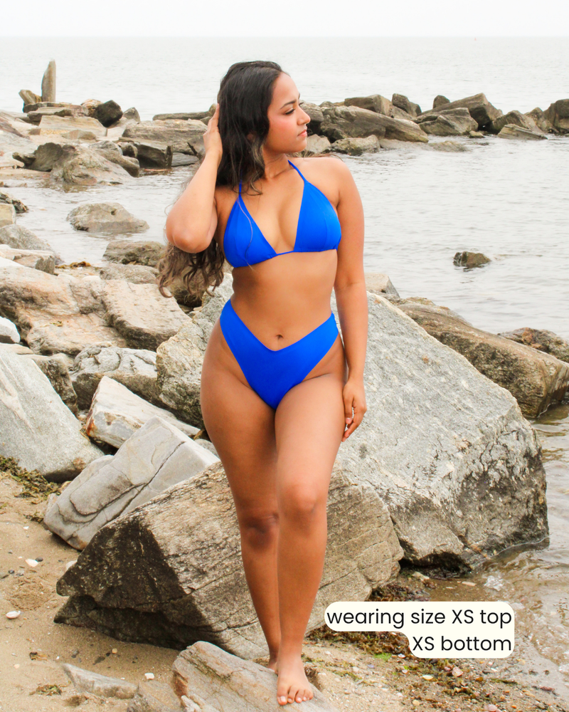 Woman wearing a blue bikini standing on rocks by the water