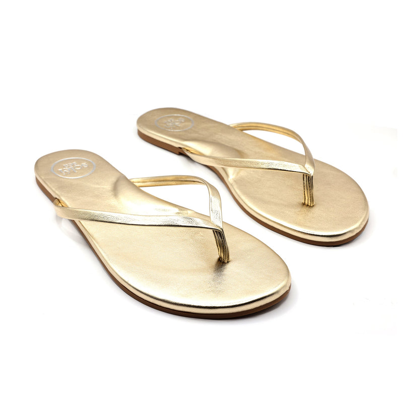 Pair of gold metallic flip-flop sandals, thong style, angled view.