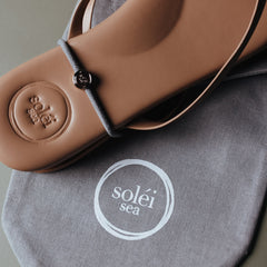 Tan leather thong sandal with embossed circular logo on the heel and white printed logo on the footbed.