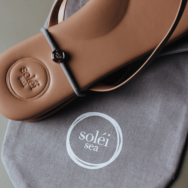 Tan leather slide sandal with round medallion and circular sticker reading 'solei'.