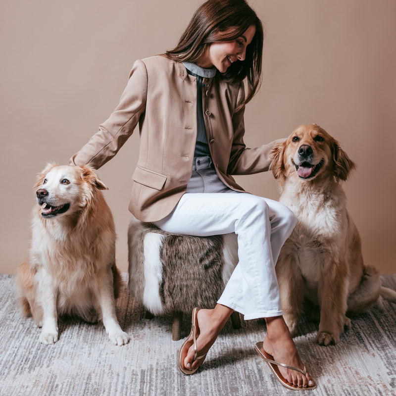 Woman seated on a wooden step with two golden retrievers, smiling and petting them, wearing flip-flops