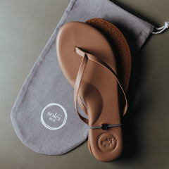 Tan leather thong sandal with embossed circular logo on the heel and white printed logo on the footbed.