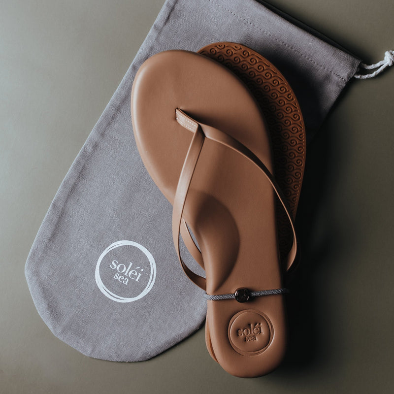 Tan leather thong sandal with embossed circular logo on the heel and white printed logo on the footbed.