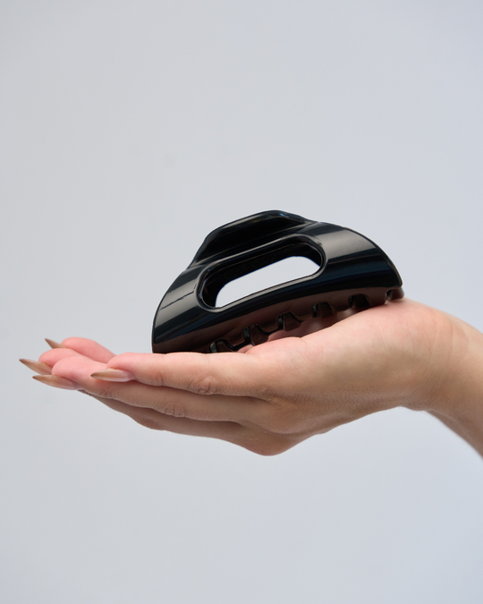 Black plastic Cozy Clip hair clip resting in an open palm
