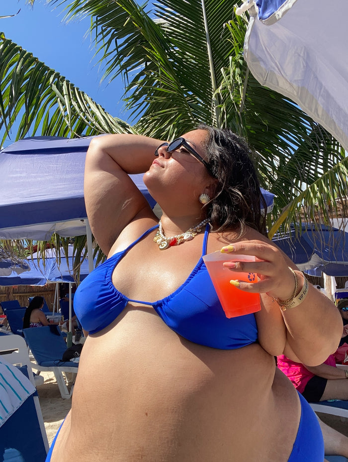 Woman in blue bikini and sunglasses holding a red drink cup under a palm tree.
