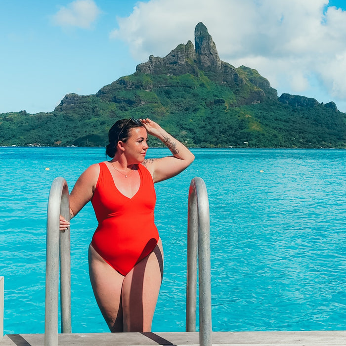 Woman in red swimsuit looking over a railing with turquoise water and a volcanic island in background