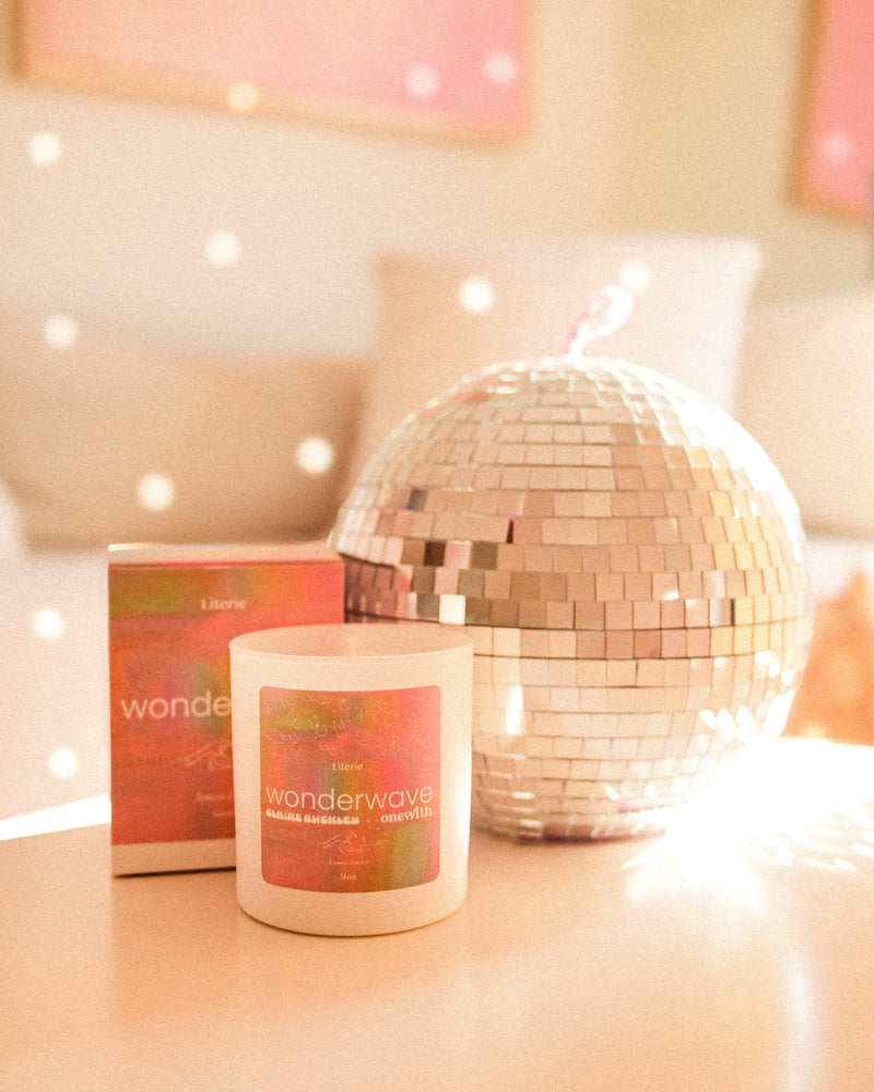 Scented candle and box labeled 'onewith x Claire Buckley Wonderwave' beside a mirrored disco ball.