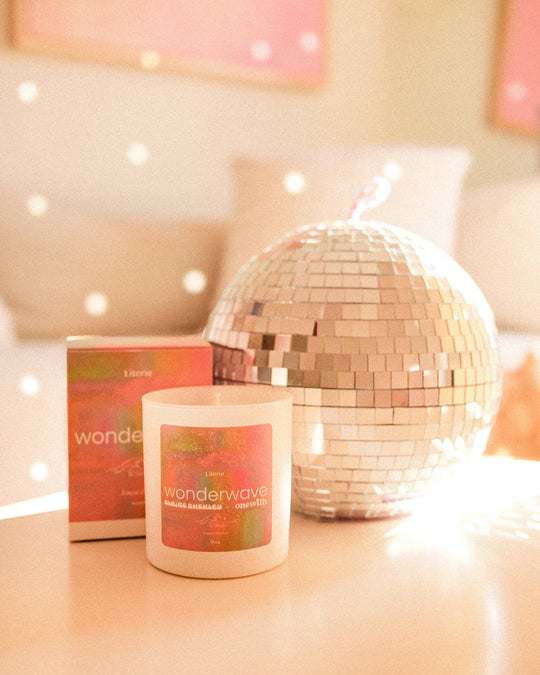 Scented candle and box labeled 'onewith x Claire Buckley Wonderwave' beside a mirrored disco ball.